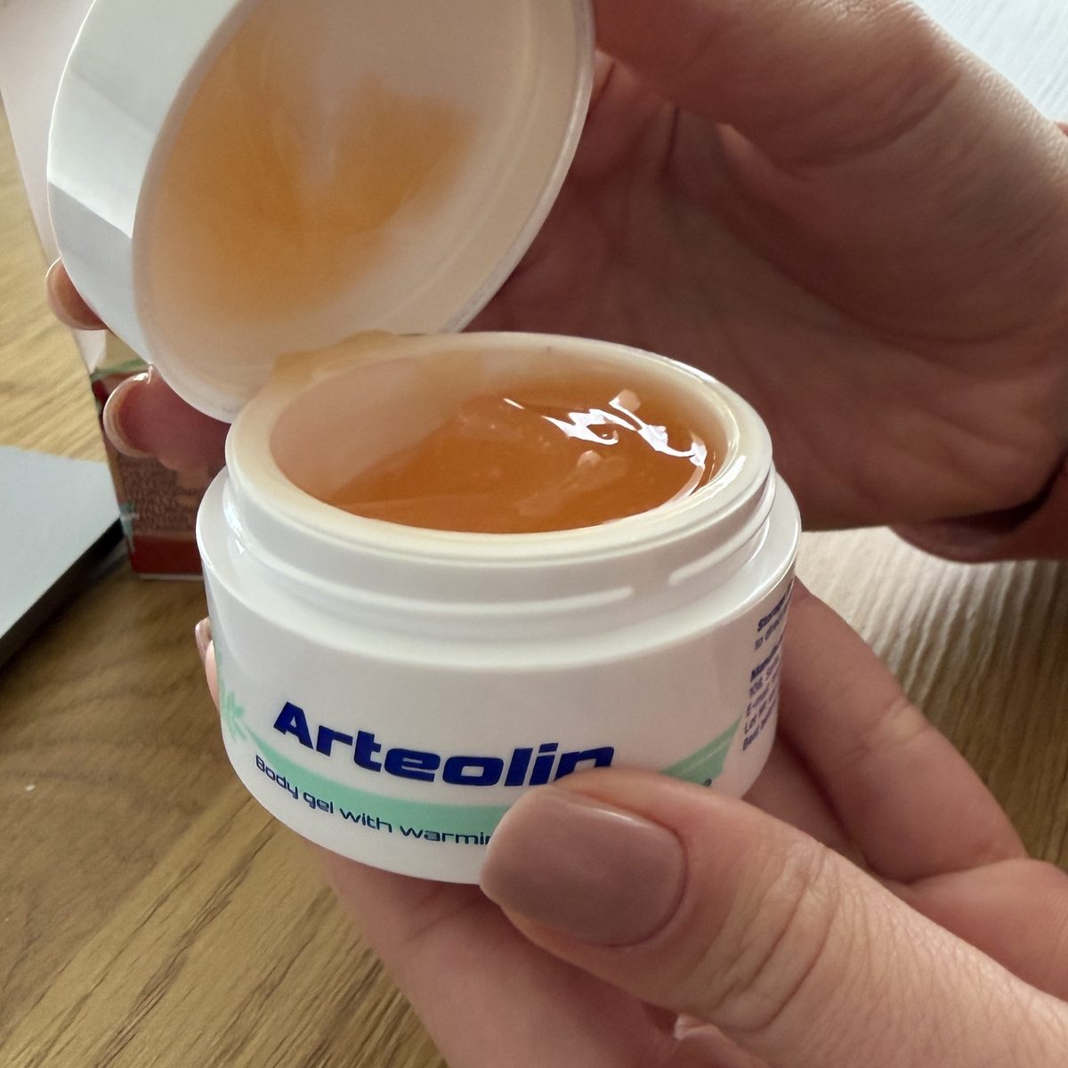 Kinyitott Arteolin tégely kézben, fényes, áttetsző, borostyánszínű géllel